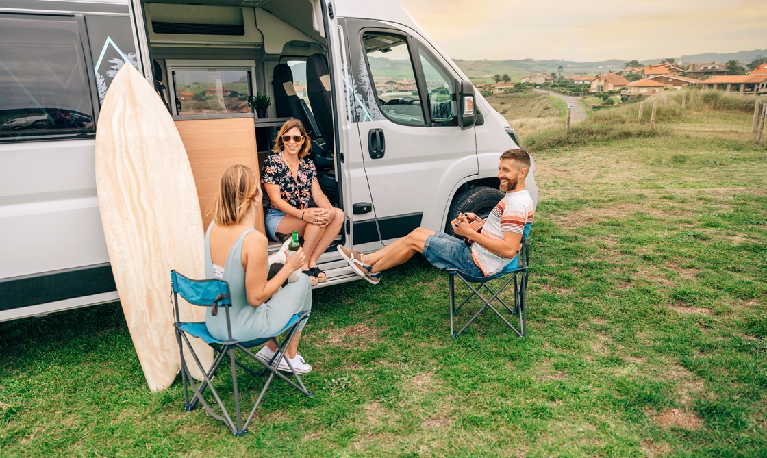 Camper lernen sich kennen und lachen gemeinsam vor ihrem Campervan mit einem Surfbrett